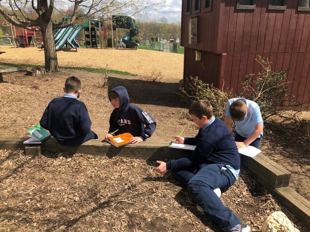 Students with clipboards sitting outside by garden box